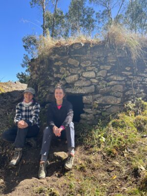 Two people sitting in front of a stone hut