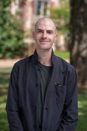 A headshot of Sasha Crawford-Holland wearing a black button up shirt.